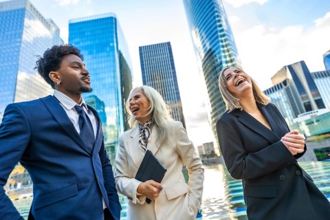 Diverse business professionals walking and laughing together outside modern corporate buildings,
