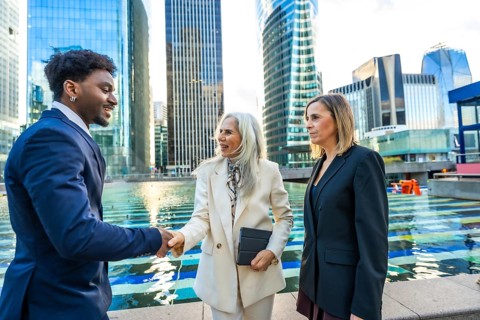 Diverse business professionals, a black man and two women, are shaking hands and discussing in a