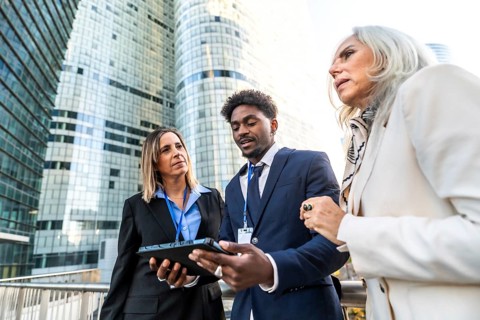 Diverse business professionals collaborating on a digital tablet, standing outdoors in front of