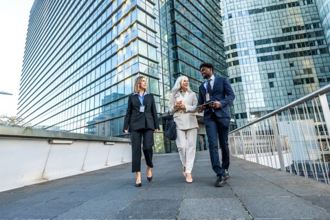 Three multi ethnic business colleagues walking and talking on a pedestrian bridge amid modern glass