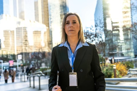 Professional businesswoman standing outdoors in a bustling city environment, wearing a suit and id