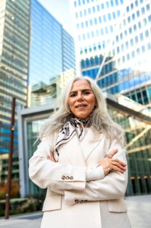 Senior businesswoman with gray hair in a cream suit stands confidently with arms crossed before