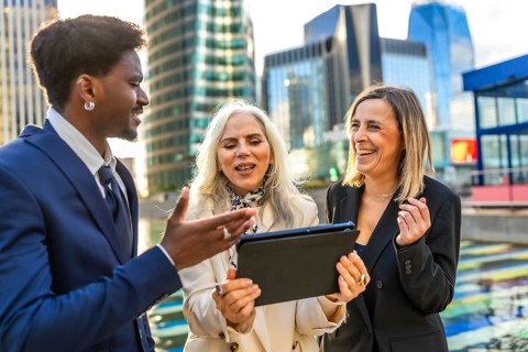 Diverse business professionals having an animated outdoor meeting, looking at a digital tablet and