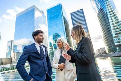 Diverse business professionals in formal attire discussing work and collaborating outdoors,
