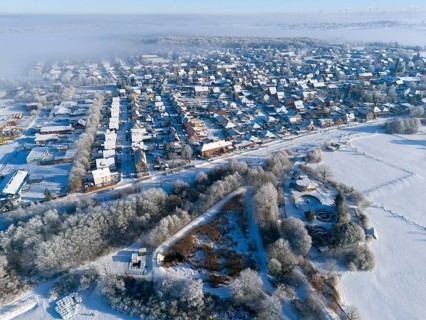 Aerial view of snowy city with fog and frost-covered fields, trees and buildings, aerial view,