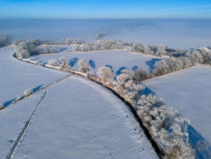 Wide winter landscape with snow-covered fields and frosty trees under a clear sky, Fuhse river,