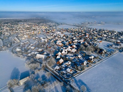 Snowy village under clear sky, sunlight reflected on white roofs and trees, aerial view, partly