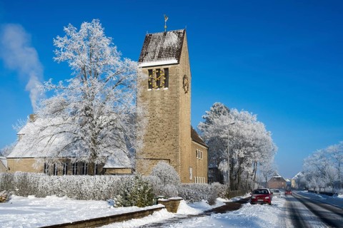 Village church with snow-covered trees against clear blue sky, car on the road, St. Mark's Church,