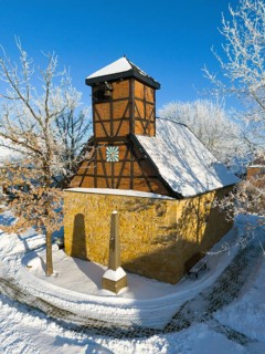 Snow-covered half-timbered church with clear structure and blue sky in cold surroundings, Old