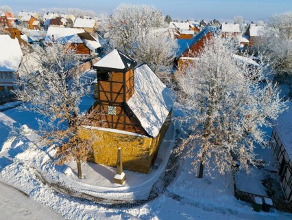 Snowy half-timbered church in wintry village against clear blue sky, aerial view, Old Chapel, 15th