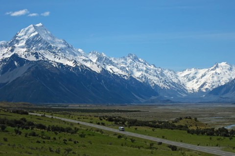 Motorhome camper van drives on a lonely country road against a huge mountain backdrop with a river