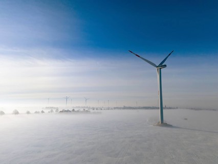 Wind turbine rises above foggy snow-covered landscape in clear blue sky, aerial view, wind turbine