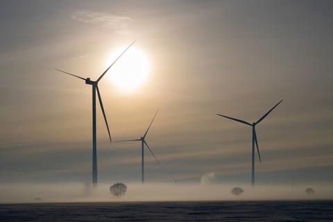 Wind turbines stand in fog under a dramatic sky at sunset, wind turbines between Solschen and