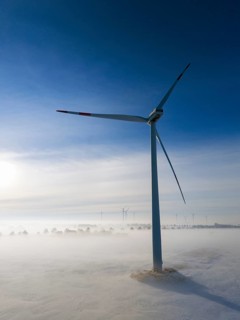 A wind turbine stands out in a snowy, foggy landscape, surrounded by soft morning light and clear