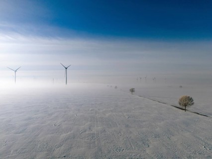 Wide snow-covered plain with wind turbines in fog under blue sky, aerial view, wind turbine and