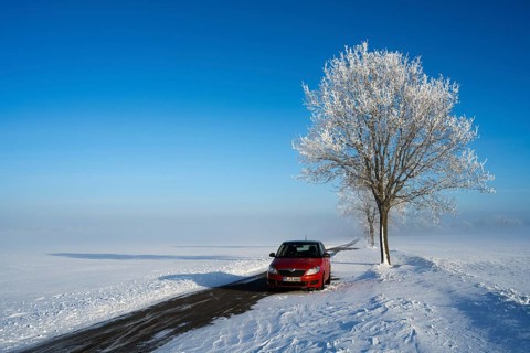 Red car parked next to a snow-covered tree on a lonely road under bright blue sky, Skoda Fabia and