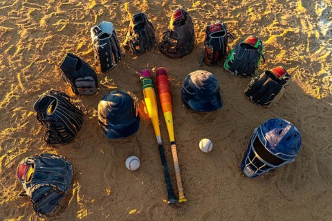 Baseball bats, gloves, helmets and catcher's mask arranged in a circle on a sandy field at sunset,