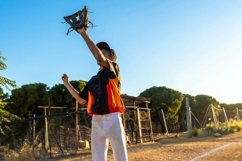 Young boy in baseball uniform and cap catches a ball with his glove on a sunny dirt field, focused