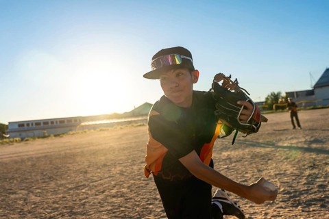 Young baseball player throwing a pitch, wearing a cap and sports goggles, with a baseball glove on
