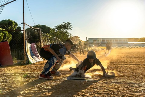 Young baseball player sliding into base on dusty infield as catcher reaches to tag him, dynamic