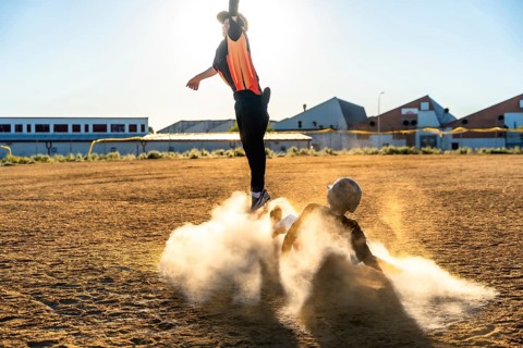Baseball players engaging in a dynamic game, one jumping to avoid a slide while the other creates a