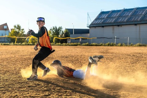 Young baseball players competing on a dusty field, one sliding head first into a base while an