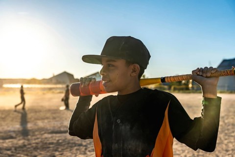 Young male baseball player holding a bat over his shoulder, wearing a cap and jersey, standing on a