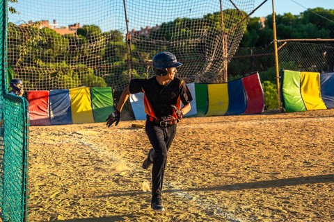 Young baseball player, wearing a helmet and uniform, running with determination on the dirt field
