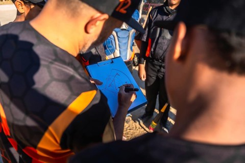 Baseball coach in uniform drawing game strategy on clipboard while explaining plays to youth team