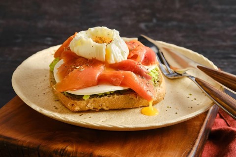 A plate holds a piece of toast topped with sliced smoked salmon and a poached egg. Yellow yolk runs