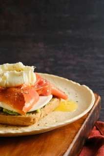 A plate holds a piece of toast topped with salmon, cream, and herbs. The setting appears casual and