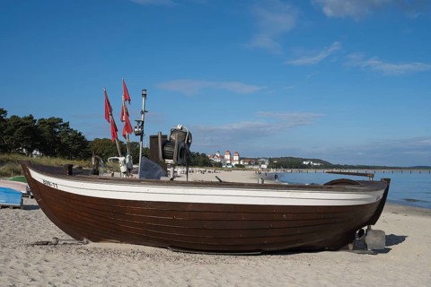 Boat with fishing flags is lying on a sandy beach, behind the spa hotel, blue sky, Binz, seaside