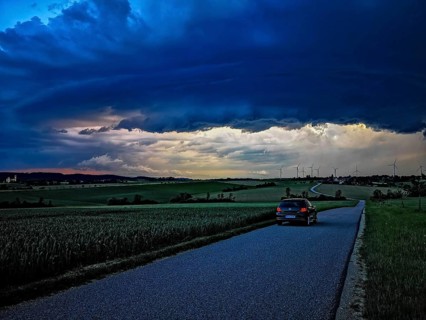 Supercell, car driving on a small road towards an approaching thunderstorm, impressive and