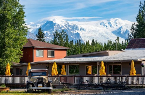 Vintage car and historic building in front of mountain landscape with Kennicott Glacier, McCarthy,