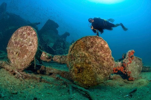 Underwater photo of diver swimming over Boonsung wreck looking at parts of former sunken tin