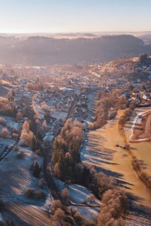 Aerial view of a snowy village in a hilly landscape at sunrise with long shadow plays, Glatten,