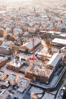 City view in winter with snow-covered roofs and a red construction crane in front of a snowy