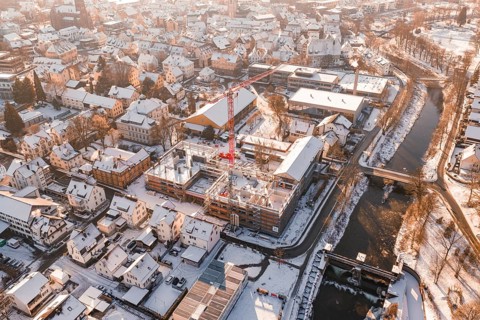 Snowy town with red construction crane standing on a construction site near a river, Zellerschule
