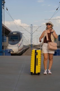 Adult woman walking on a modern train platform with a yellow suitcase, waiting for departure. Solo