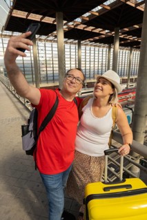 Smiling adult travel couple taking a selfie and looking at a smartphone while standing inside a