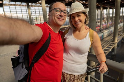 Happy adult travel couple taking a selfie and looking at the camera while standing inside a modern