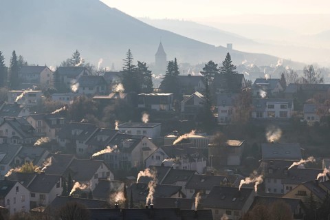 Extensive village panorama with smoking chimneys and hills in the morning haze, symbolic image,