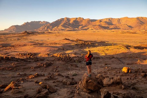Young woman standing in desert landscape with Brandberg in morning light, at sunrise, Erongo,