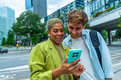 Business colleagues standing outdoors in a city, happily sharing and viewing content together on a