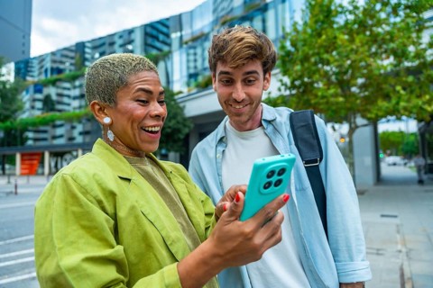 Diverse colleagues standing in a city, happily sharing and viewing content on a smartphone,
