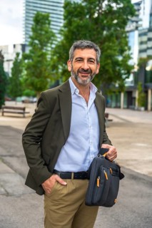 Confident mature businessman with beard and suit jacket smiling at camera, holding a messenger bag