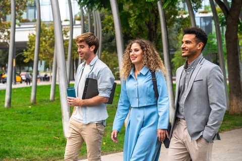 Three diverse business professionals, two men and one woman, walking and conversing outdoors in a