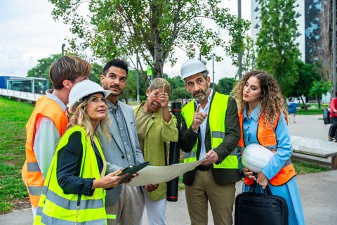 Architects, engineers, and construction colleagues in hard hats and vests discussing blueprints and
