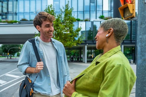 Two diverse business colleagues laugh and chat while walking on a city street, sharing a friendly,