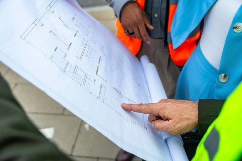 Engineers and architects in safety vests analyzing and discussing a detailed building blueprint,